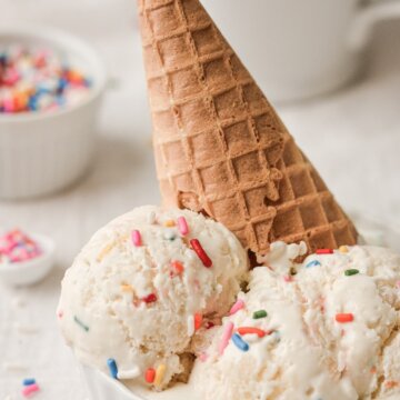 Scoops of birthday cake ice cream topped with sprinkles and a waffle cone.
