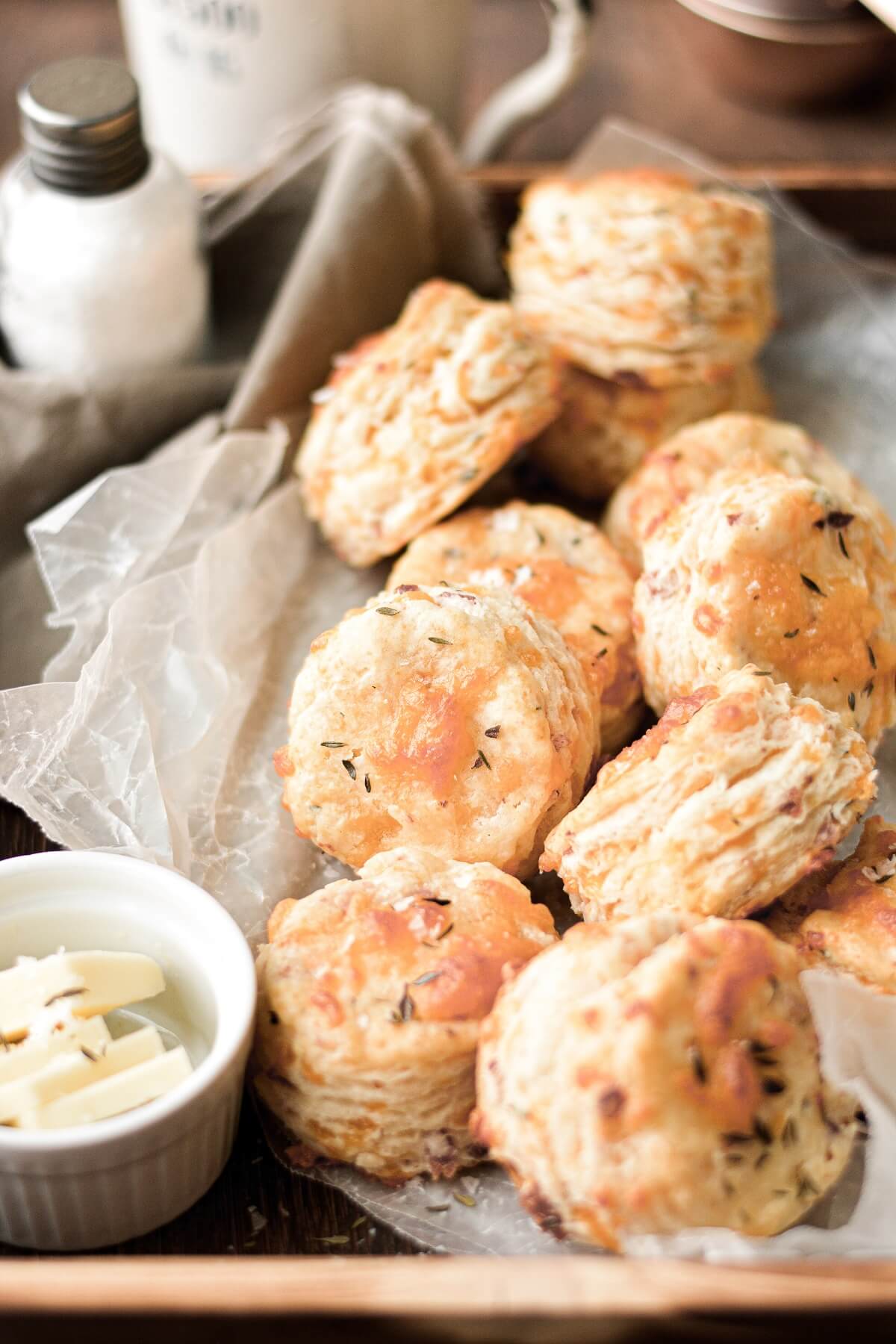 Cheesy herb biscuits arranged on a wooden tray with butter and salt.