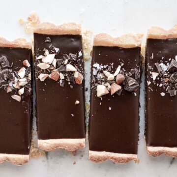Slices of chocolate almond tart, sprinkled with chopped chocolate and almonds.