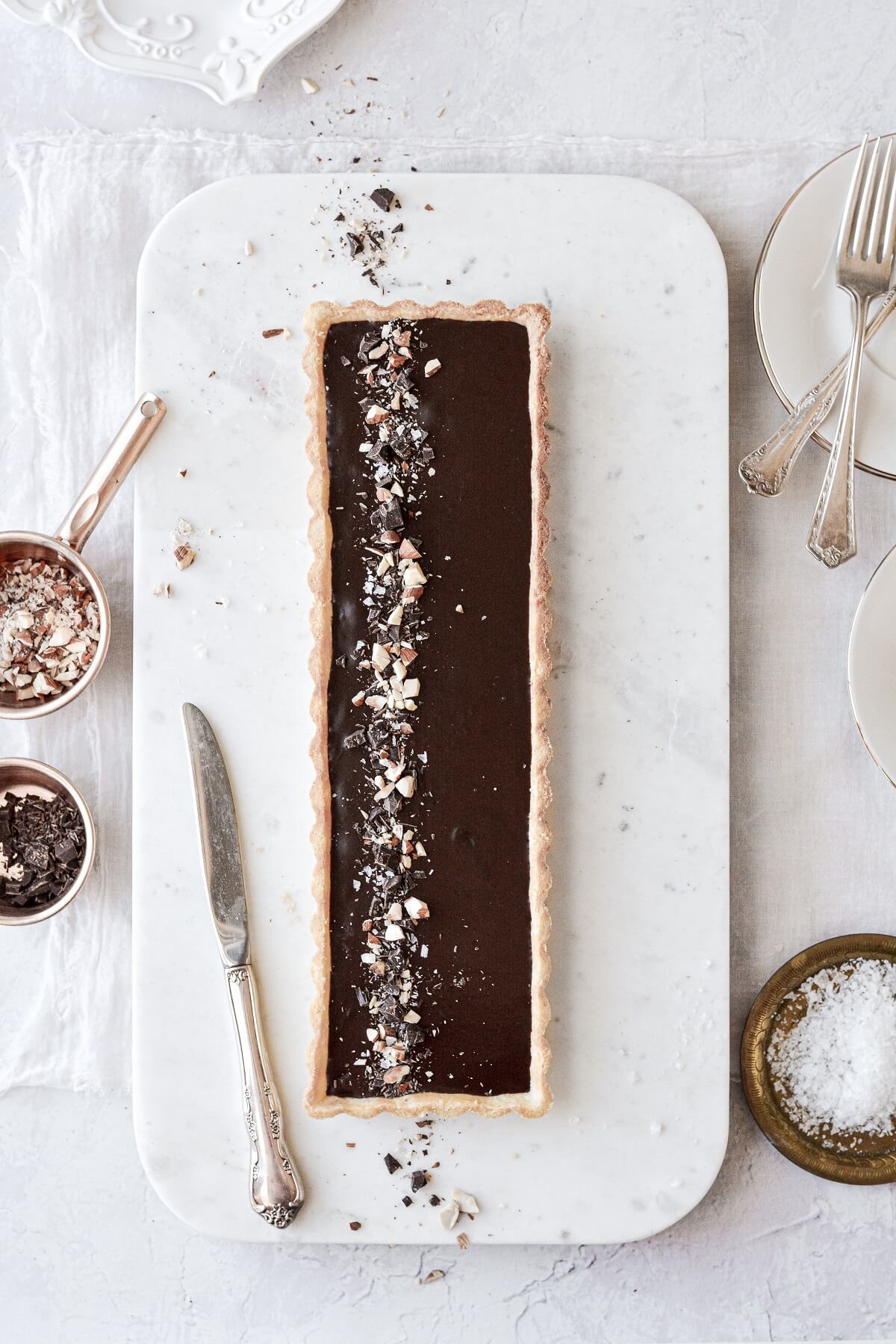 Chocolate almond tart, sprinkled with chopped chocolate and almonds, on a marble serving board.