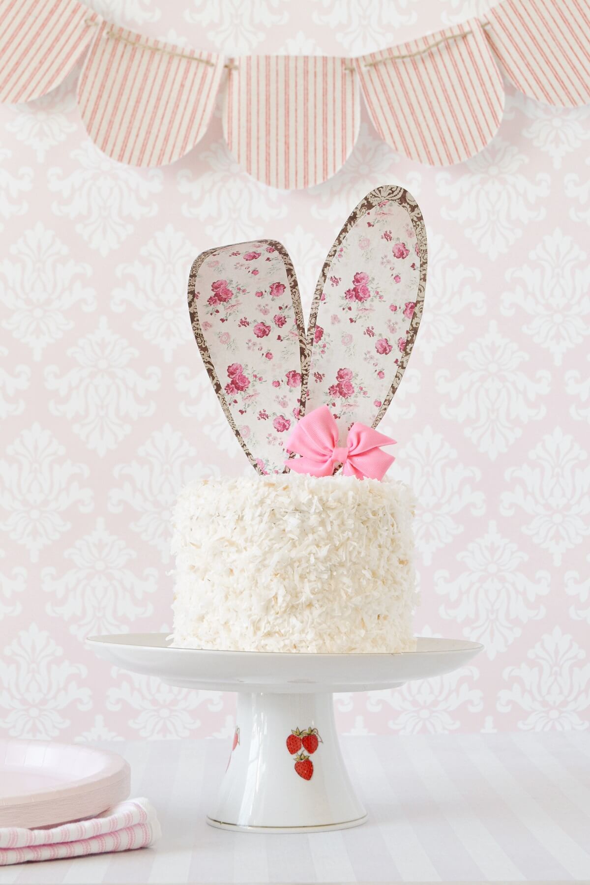 An Easter bunny coconut cake with paper floral ears, and a pink candy bow.