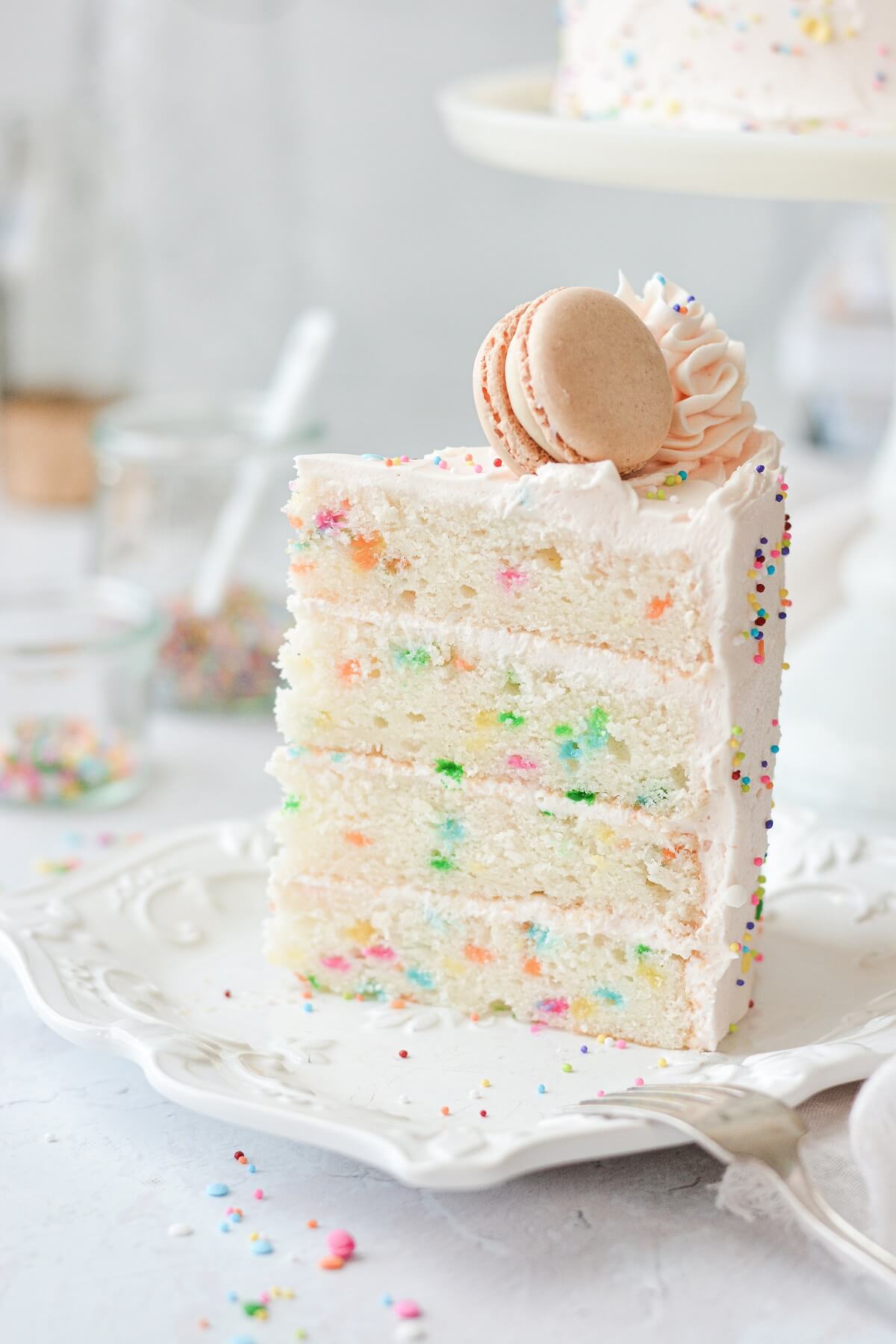 A slice of funfetti cake, topped with a macaron.