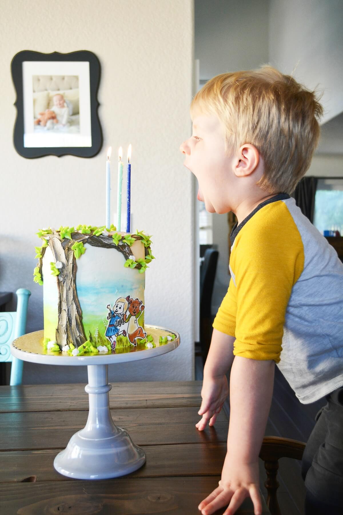 A little boy, blowing out three birthday candles on a Goldie and Bear cake.
