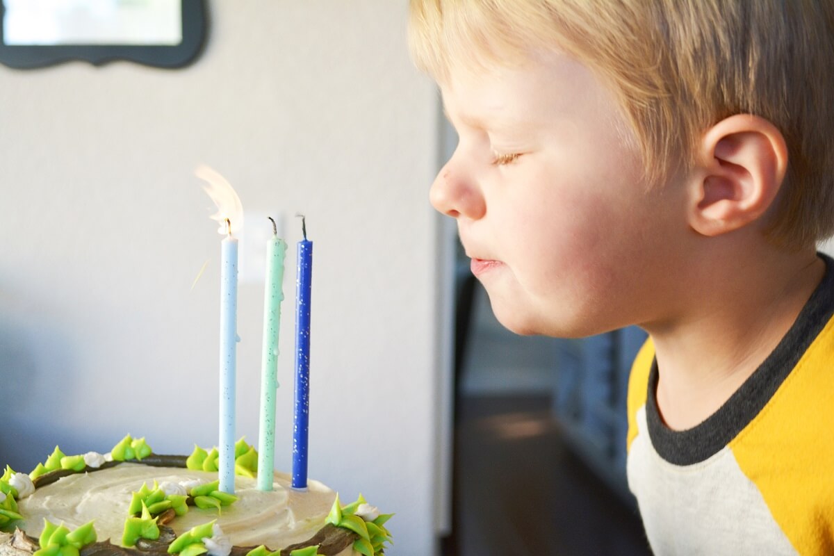 A little boy, blowing out three birthday candles on a Goldie and Bear cake.