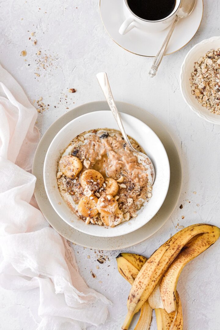 A bowl of oatmeal topped with caramelized bourbon bananas and chopped hazelnuts.