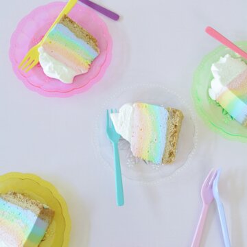 Slices of rainbow cheesecake on colorful plates.