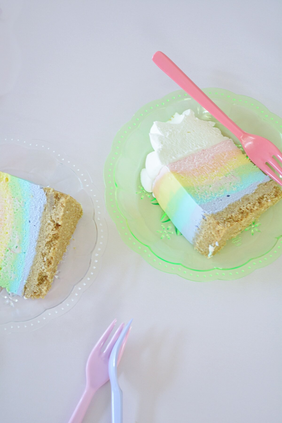 A slice of rainbow cheesecake on a green plate.