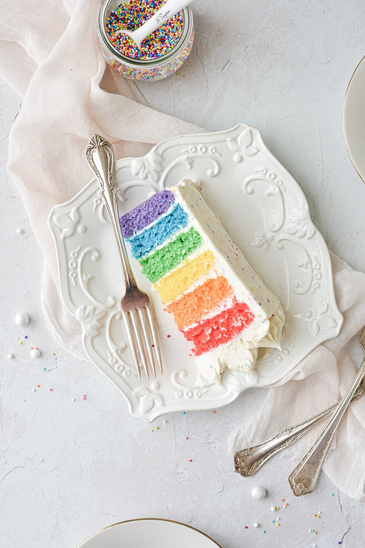 A slice of rainbow cake on a white plate.