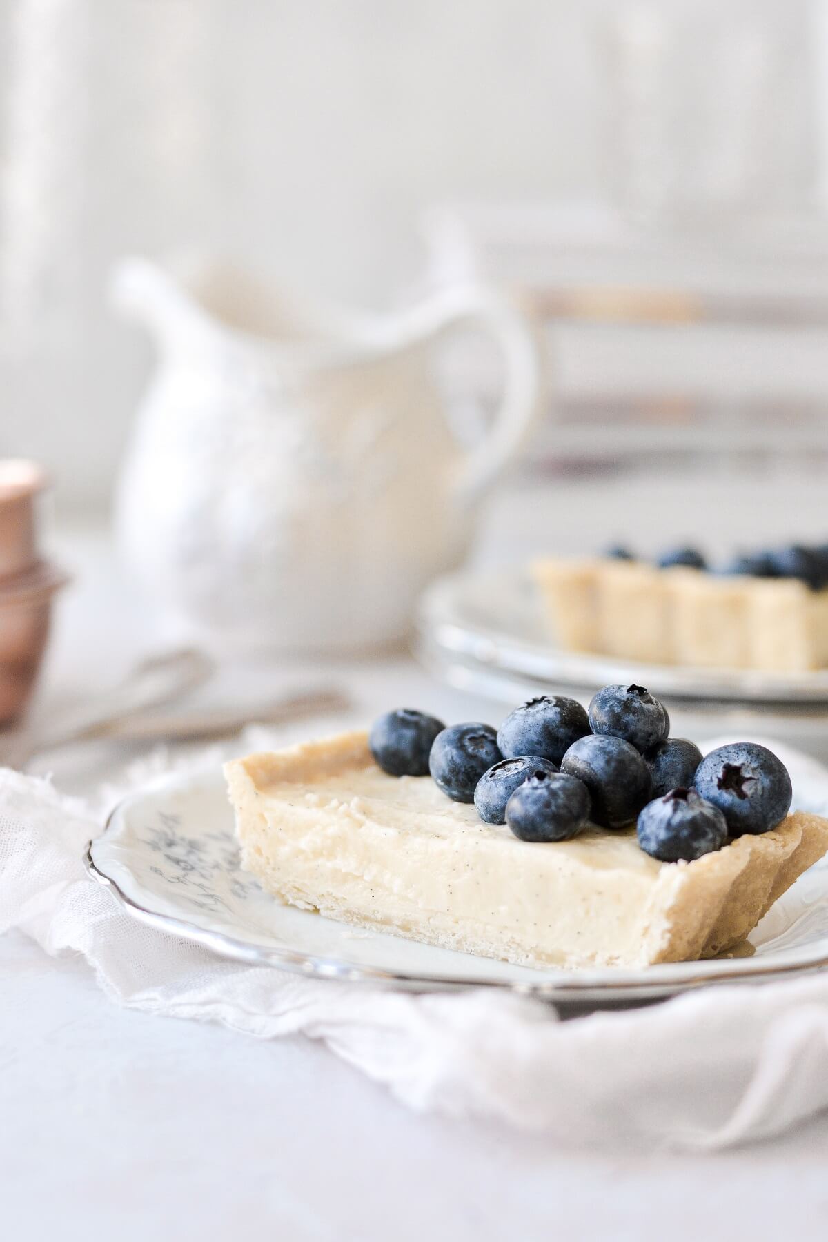A slice of vanilla bean custard tart topped with blueberries.