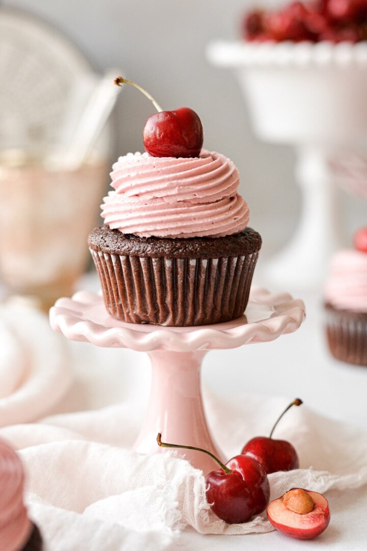 A chocolate cherry cupcake on a mini pink pedestal.