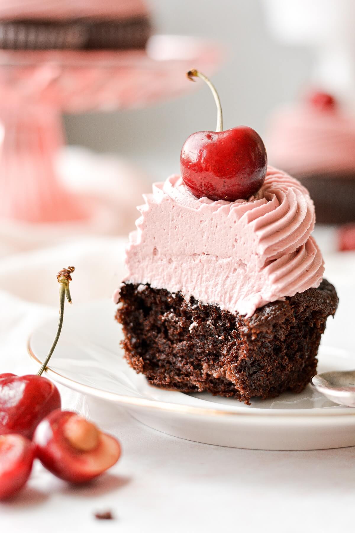 A chocolate cherry cupcake with a bite taken.
