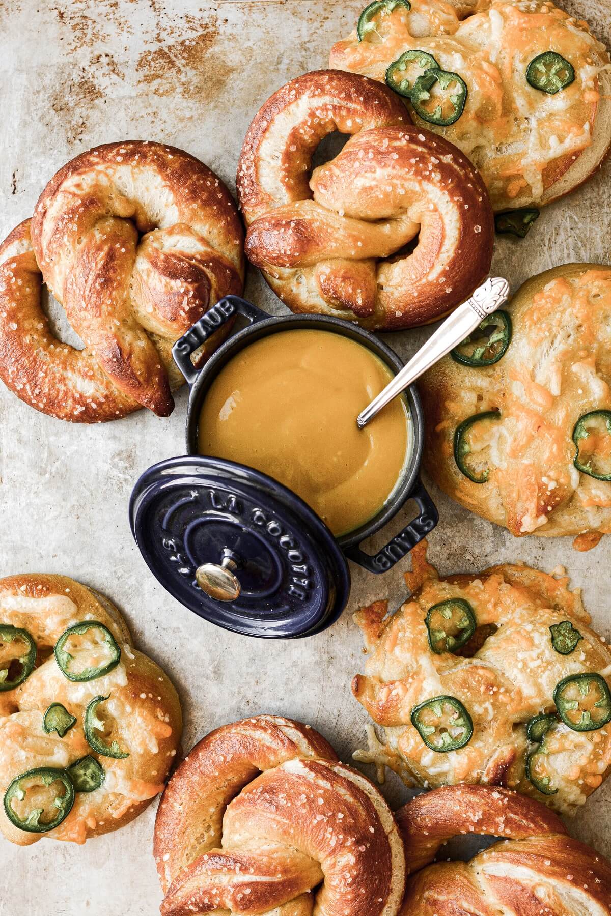 Soft pretzels on a baking sheet, with a pot of mustard for dipping.