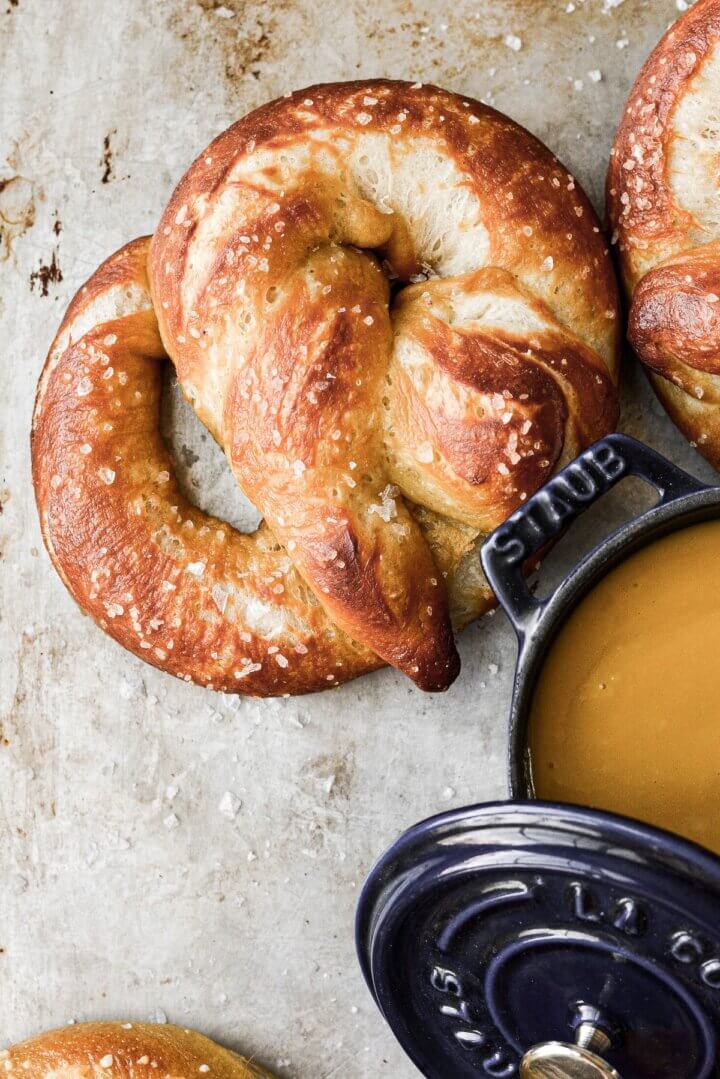 Soft pretzels on a baking sheet, with a pot of mustard for dipping.