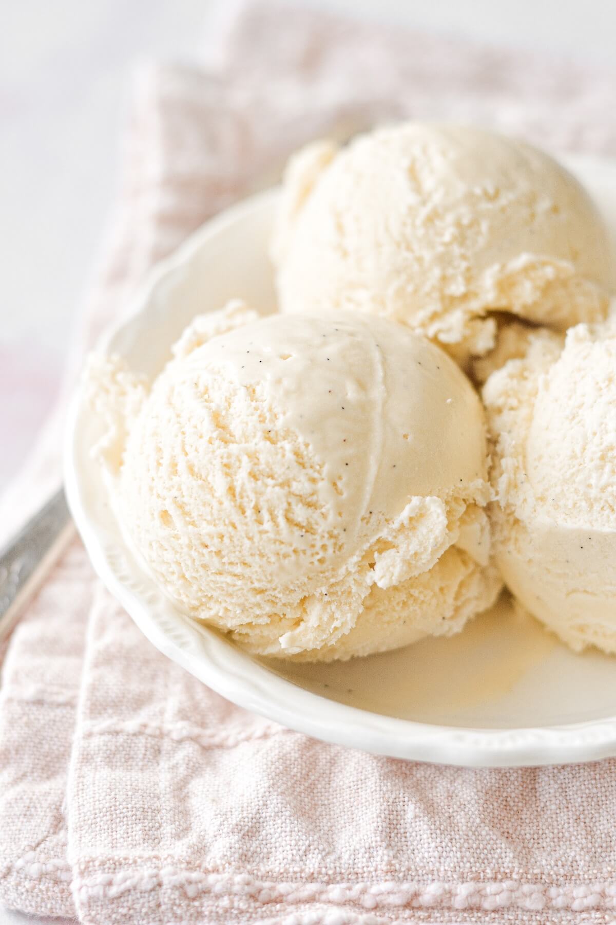 Three scoops of vanilla bean ice cream in a white bowl.