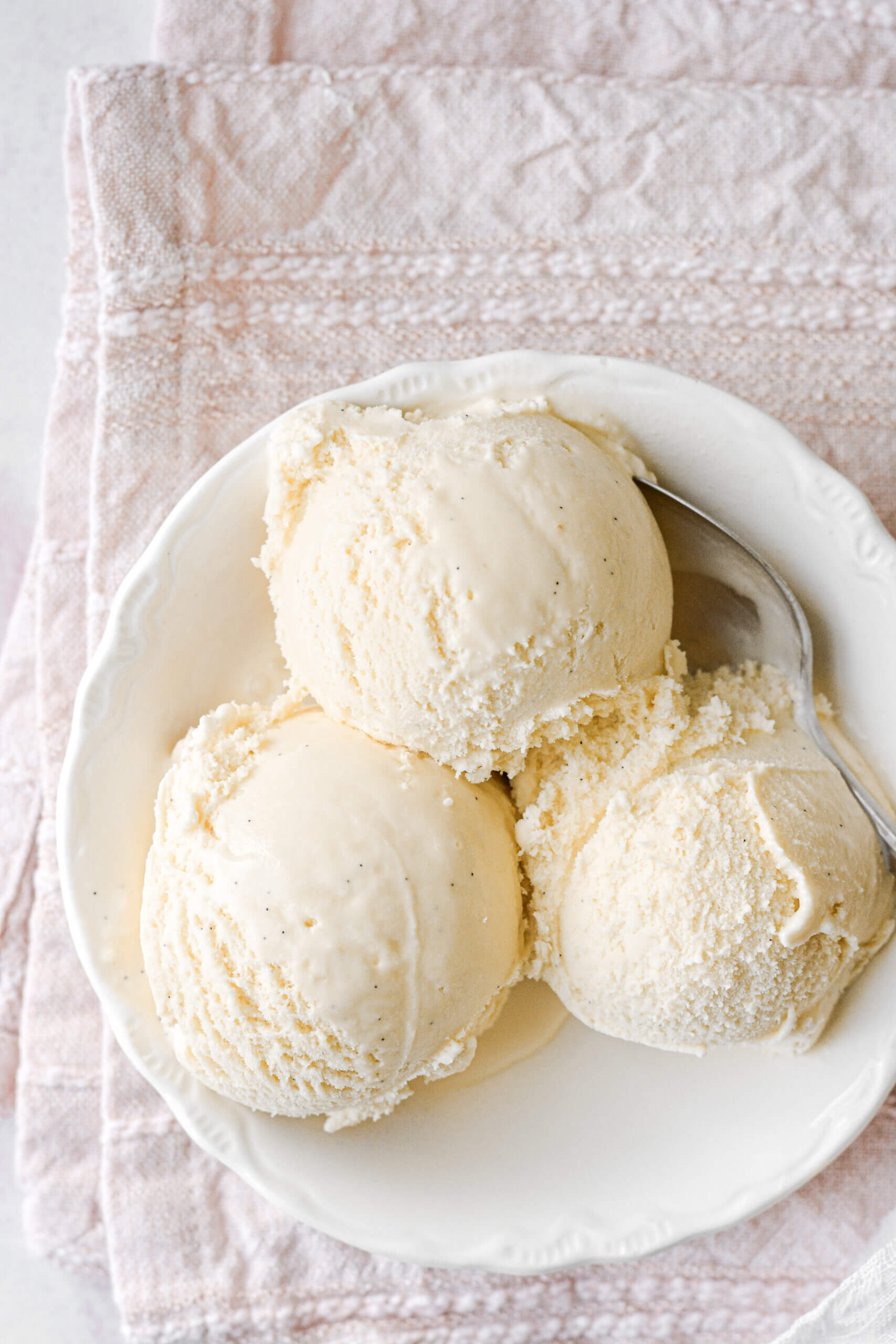 Three scoops of vanilla bean ice cream in a white bowl.