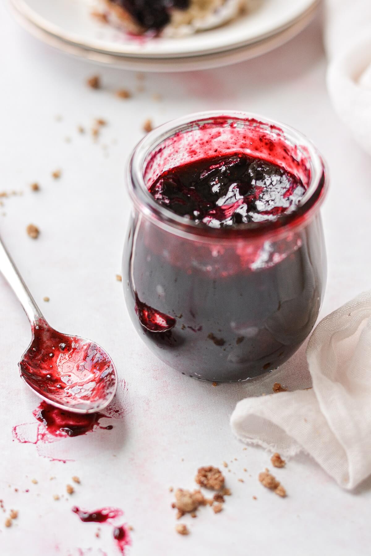 A jar of blueberry jam with a spoon resting beside the jar.