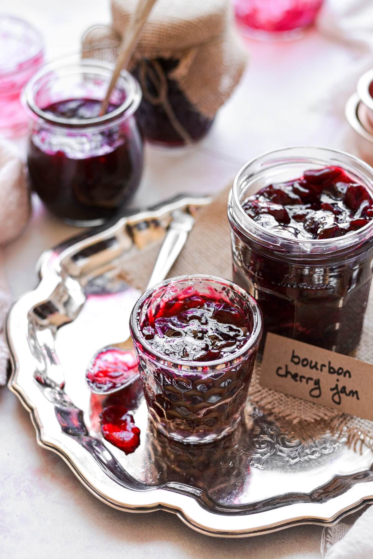 Glass jars filled with homemade bourbon cherry jam, and a spoon covered in jam.