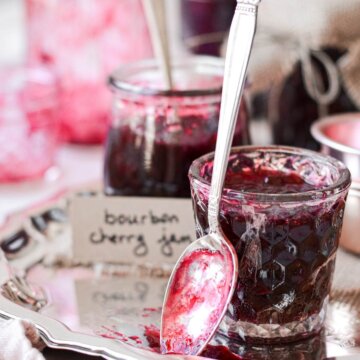 Glass jars filled with homemade bourbon cherry jam, and a spoon covered in jam.