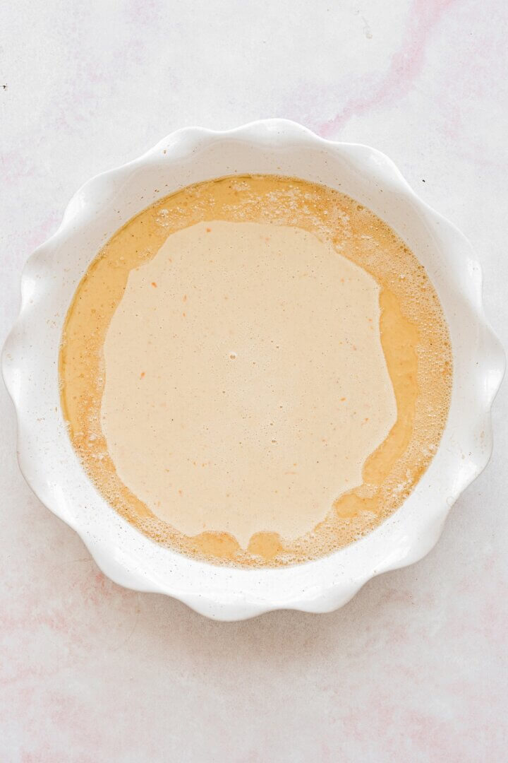 Batter for a Dutch baby in a white pie plate.