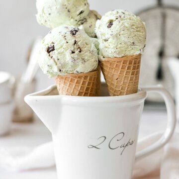 Mint chocolate chip ice cream in sugar cones, in a white measuring cup.