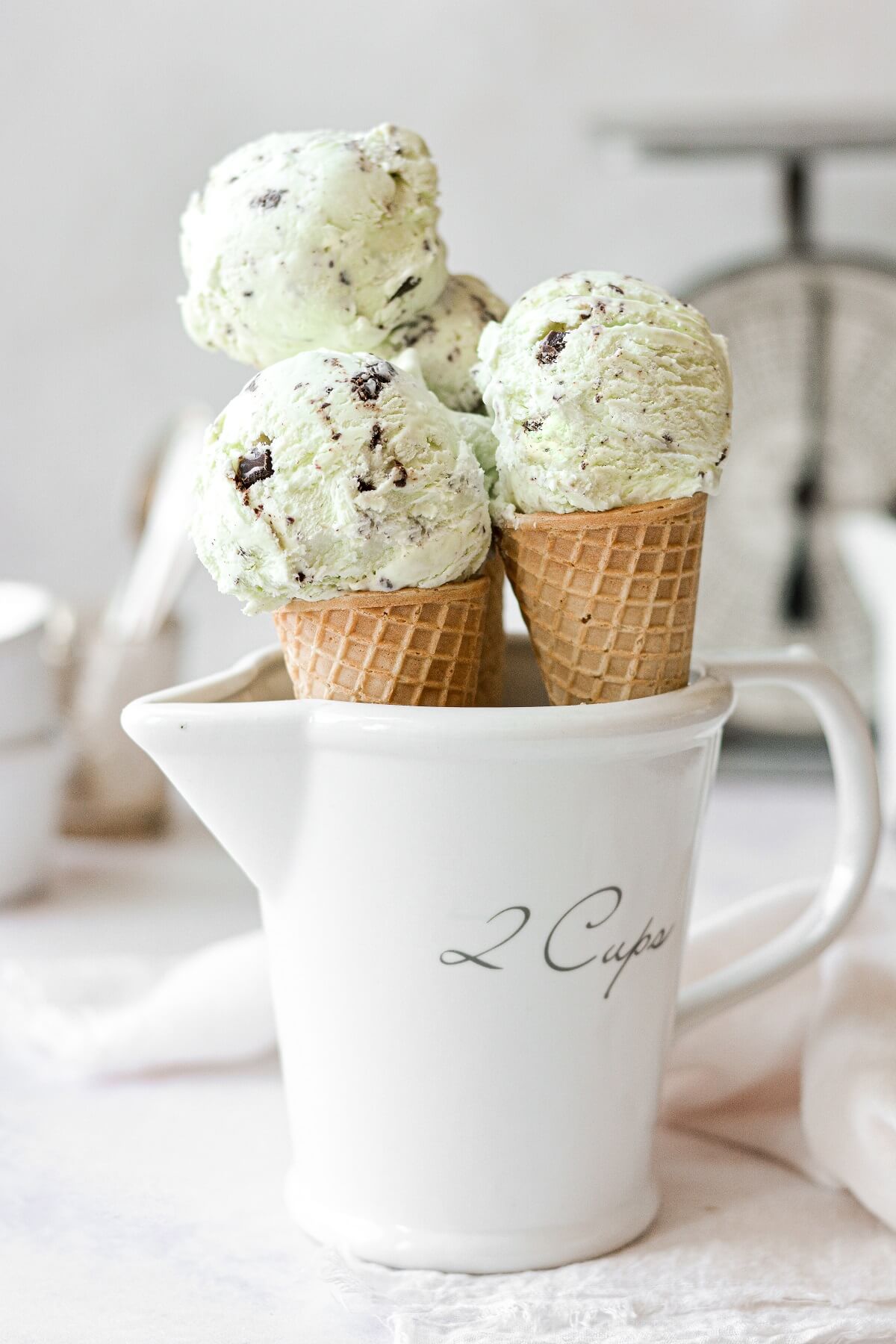Mint chocolate chip ice cream in sugar cones, in a white measuring cup.