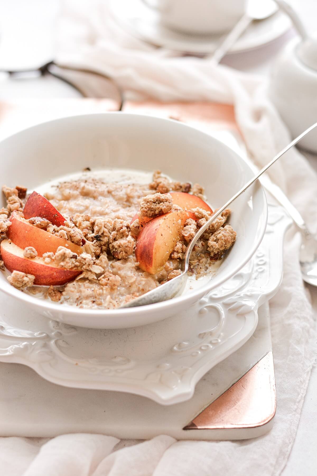 A bowl of oatmeal topped with sliced peaches and crumble topping.