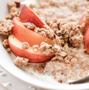A bowl of oatmeal topped with sliced peaches and crumble topping.