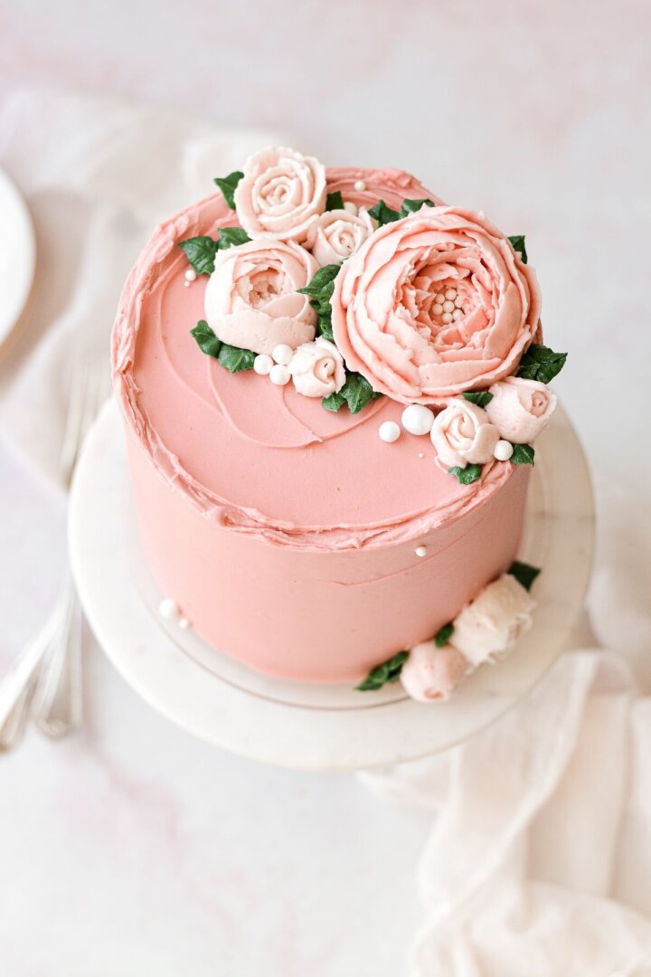 A layer cake frosted with pink buttercream and buttercream flowers.