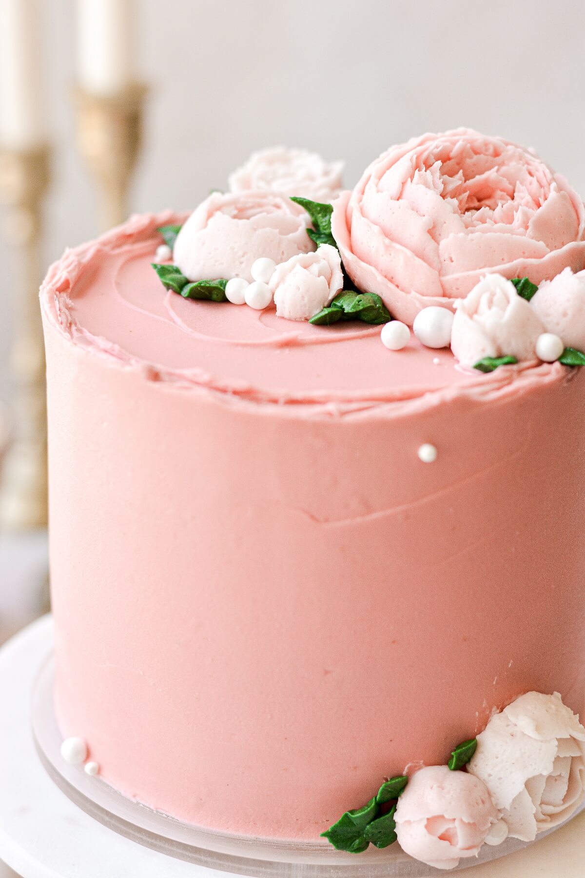A pink frosted cake with buttercream flowers and leaves.
