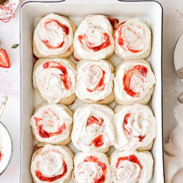Twelve strawberry rolls in a baking pan, topped with cream cheese frosting.