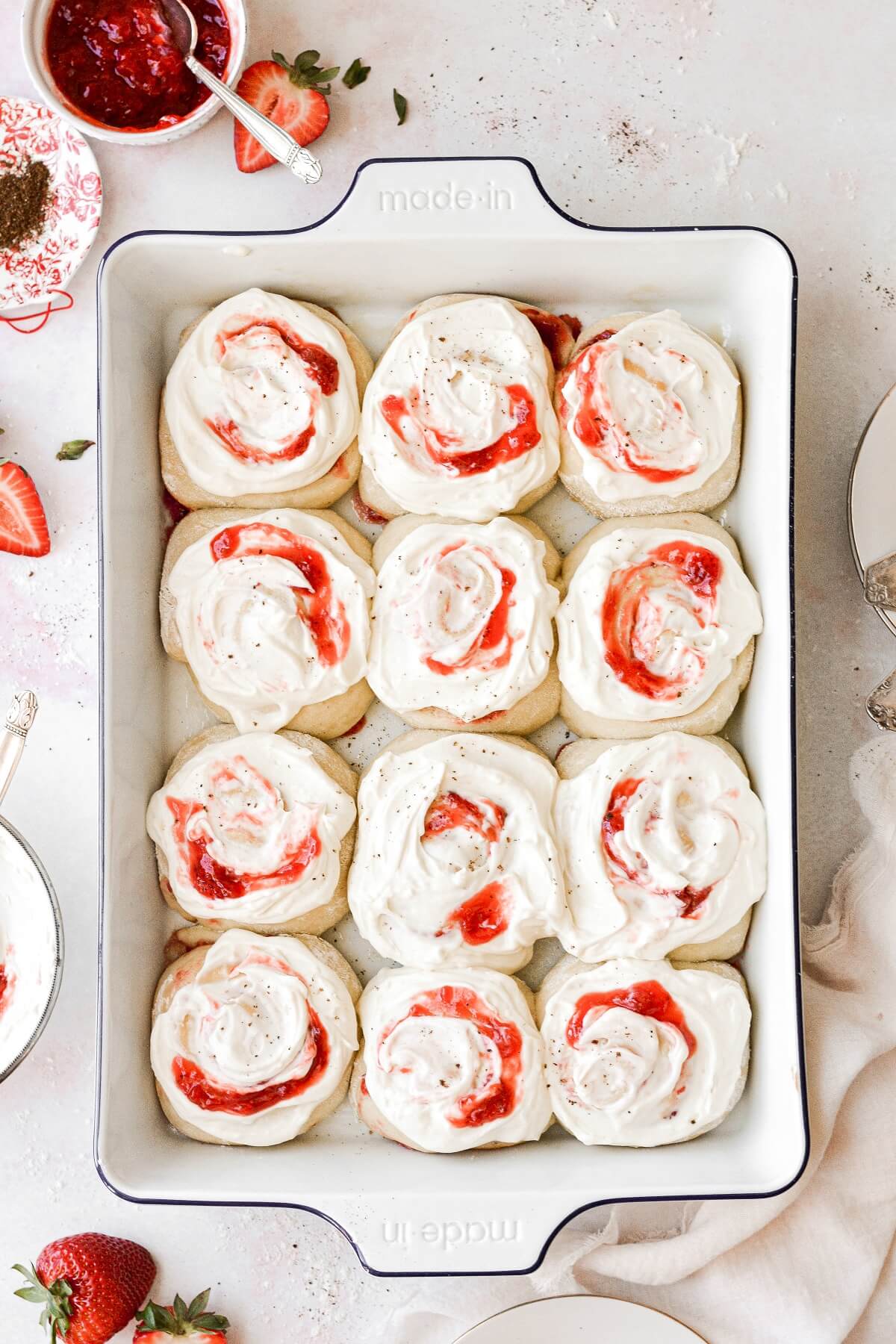Twelve strawberry rolls in a baking pan, topped with cream cheese frosting.