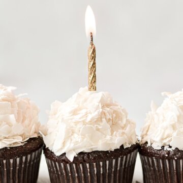 A chocolate cupcake with coconut frosting and a gold birthday candle.