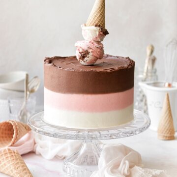 Neapolitan cake with striped buttercream and an ice cream cone cake topper.