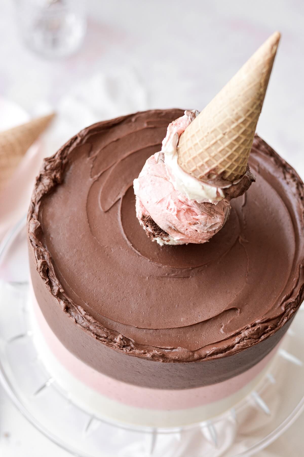 An ice cream cone sitting on top of a neapolitan cake.