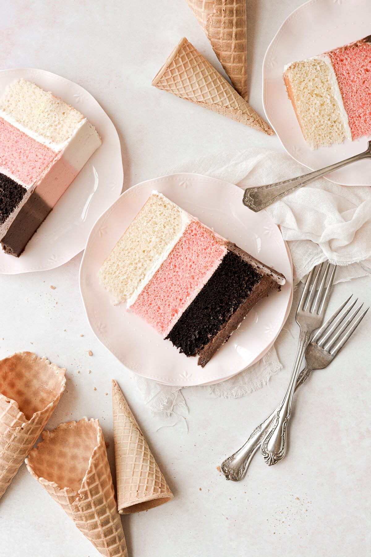 Slices of neapolitan cake, surrounded by ice cream cones.