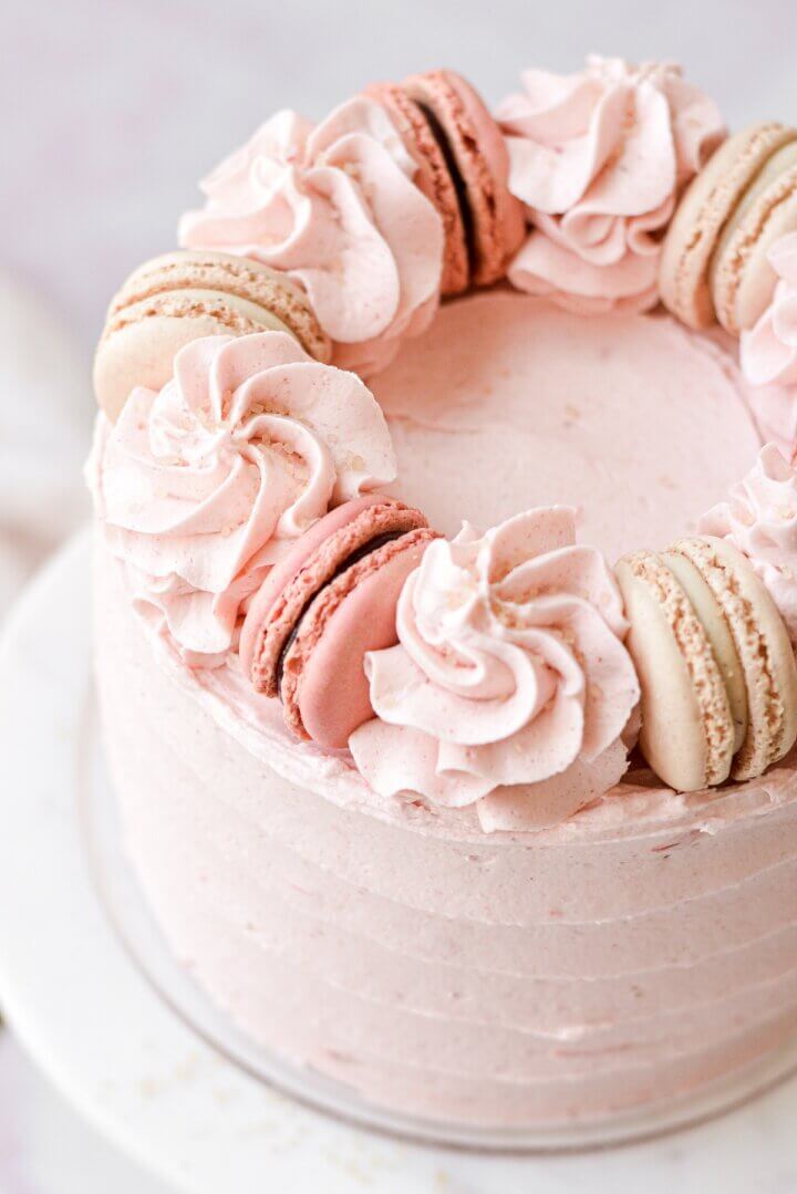The top of a strawberry almond cake with buttercream swirls and macarons.