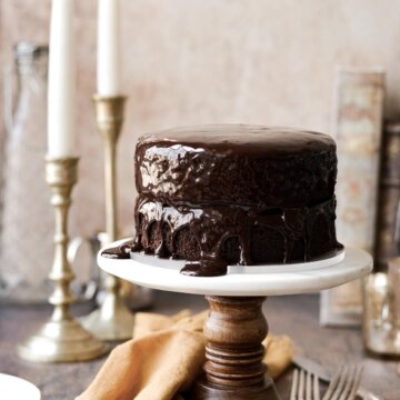 A chocolate fudge cake with ganache on a wood and marble cake stand.