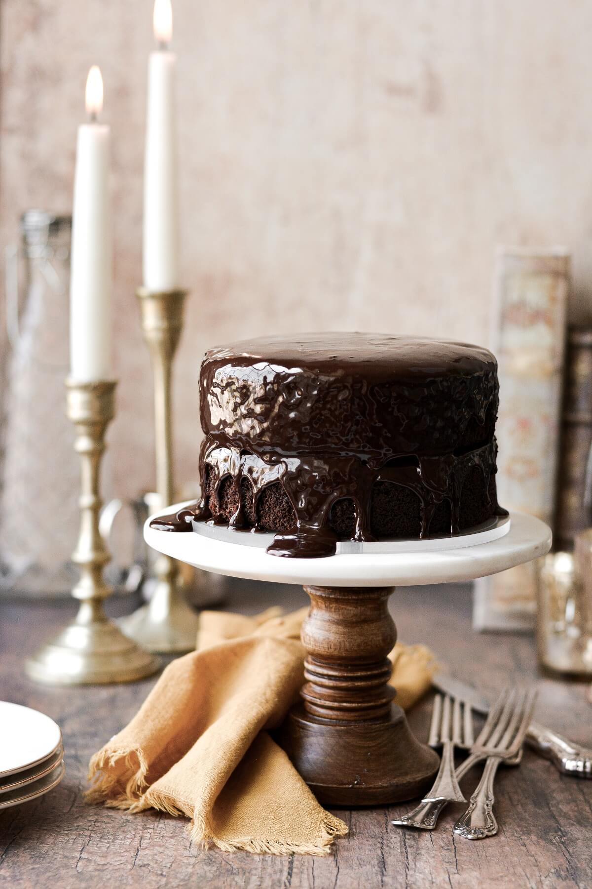 A chocolate fudge cake with ganache on a wood and marble cake stand.