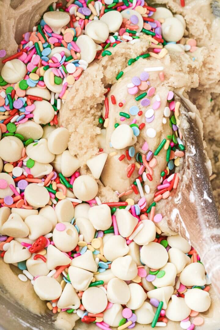 Sprinkles and white chocolate chips being mixed into cookie dough.