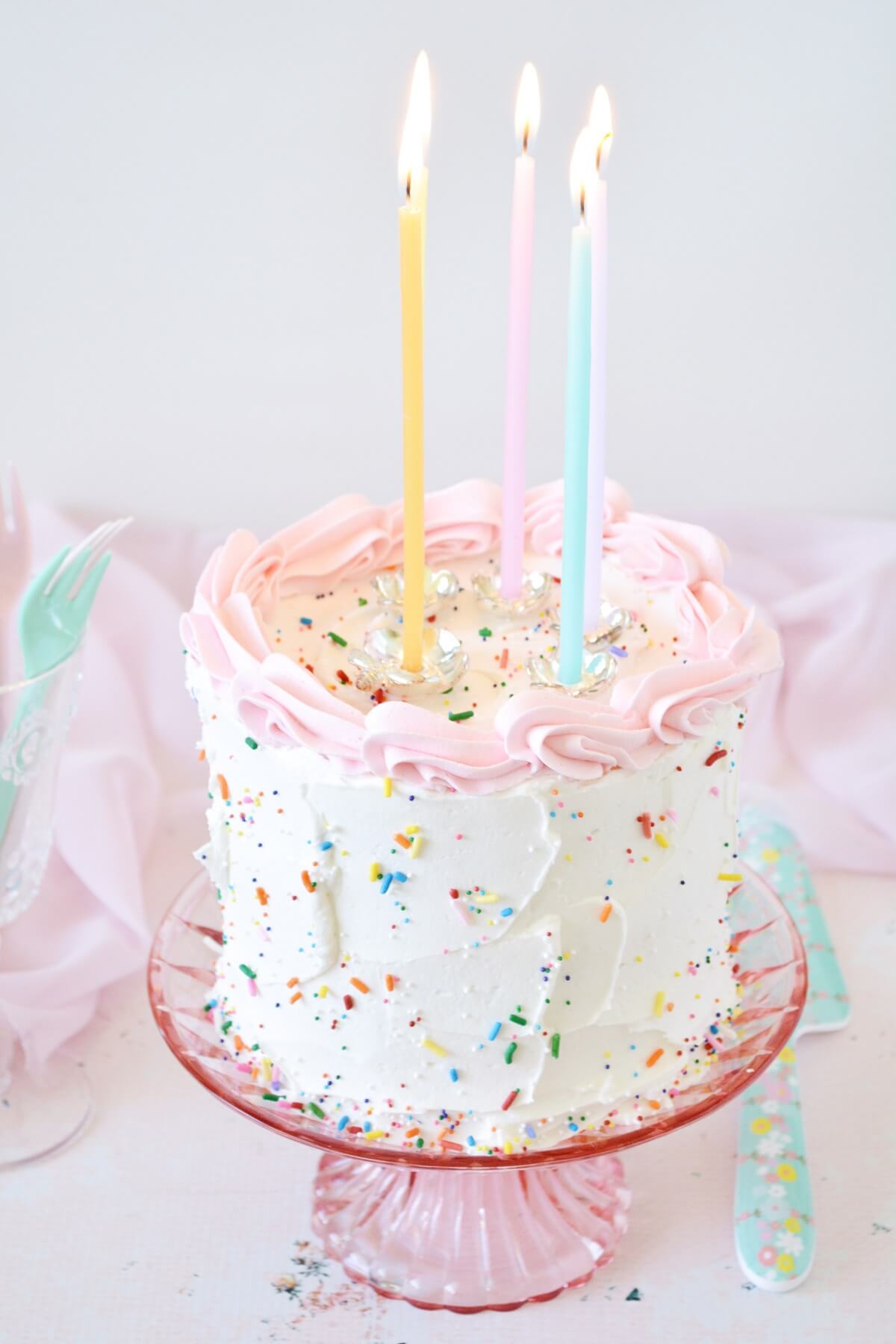 A birthday cake on a pink cake stand.