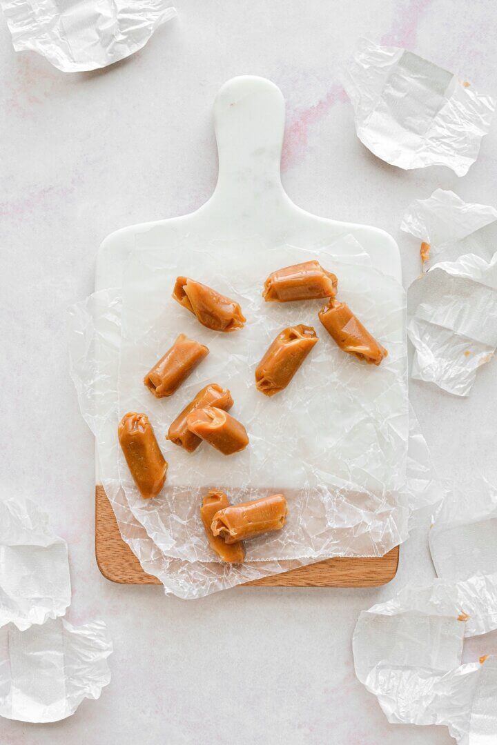 Soft caramels on a marble cutting board surrounded by candy wrappers.