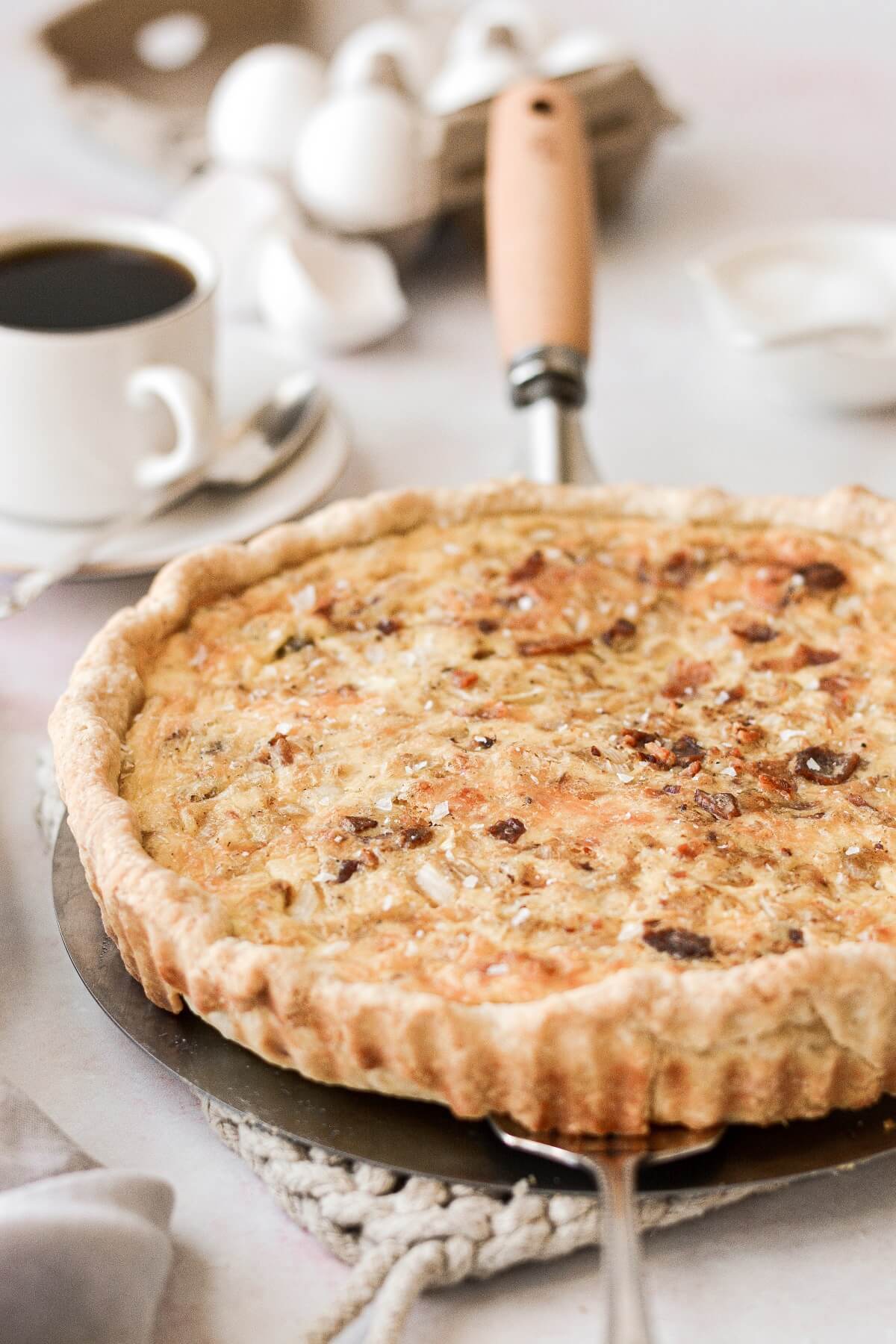 Baked quiche Lorraine next to a cup of coffee.
