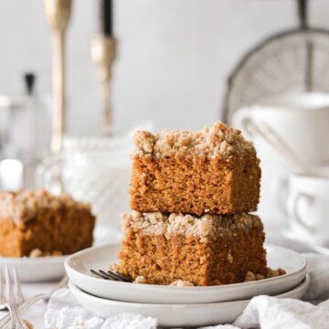 Pieces of pumpkin crumb coffee cake stacked on white plates.