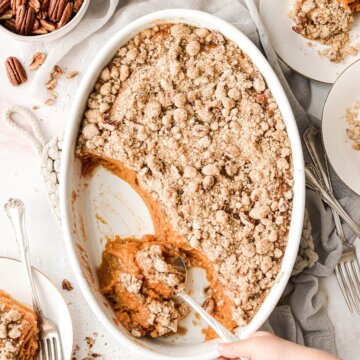 A dish of sweet potato casserole with crumb topping being scooped onto plates.