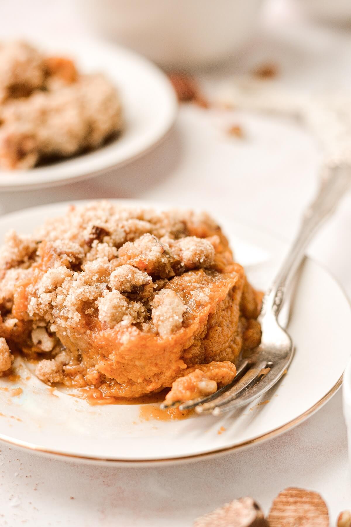 A scoop of sweet potato casserole with crumb topping on a white plate.