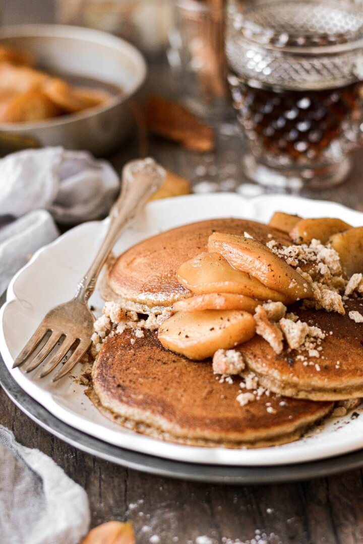 Apple cider pancakes with cinnamon apples, syrup, and cookie crumbles.