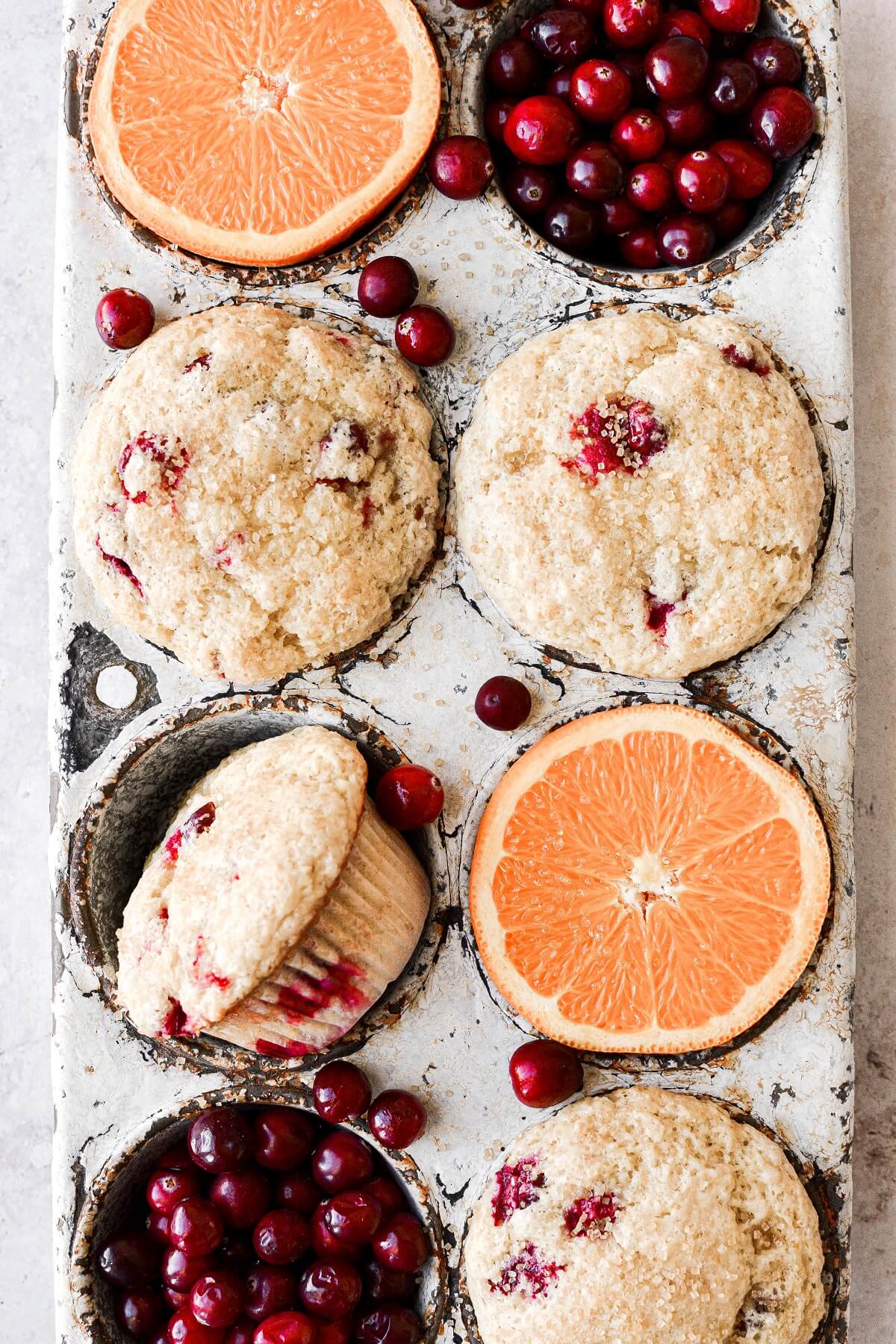 Oranges, cranberries and cranberry orange muffins, arranged in a vintage muffin tin.