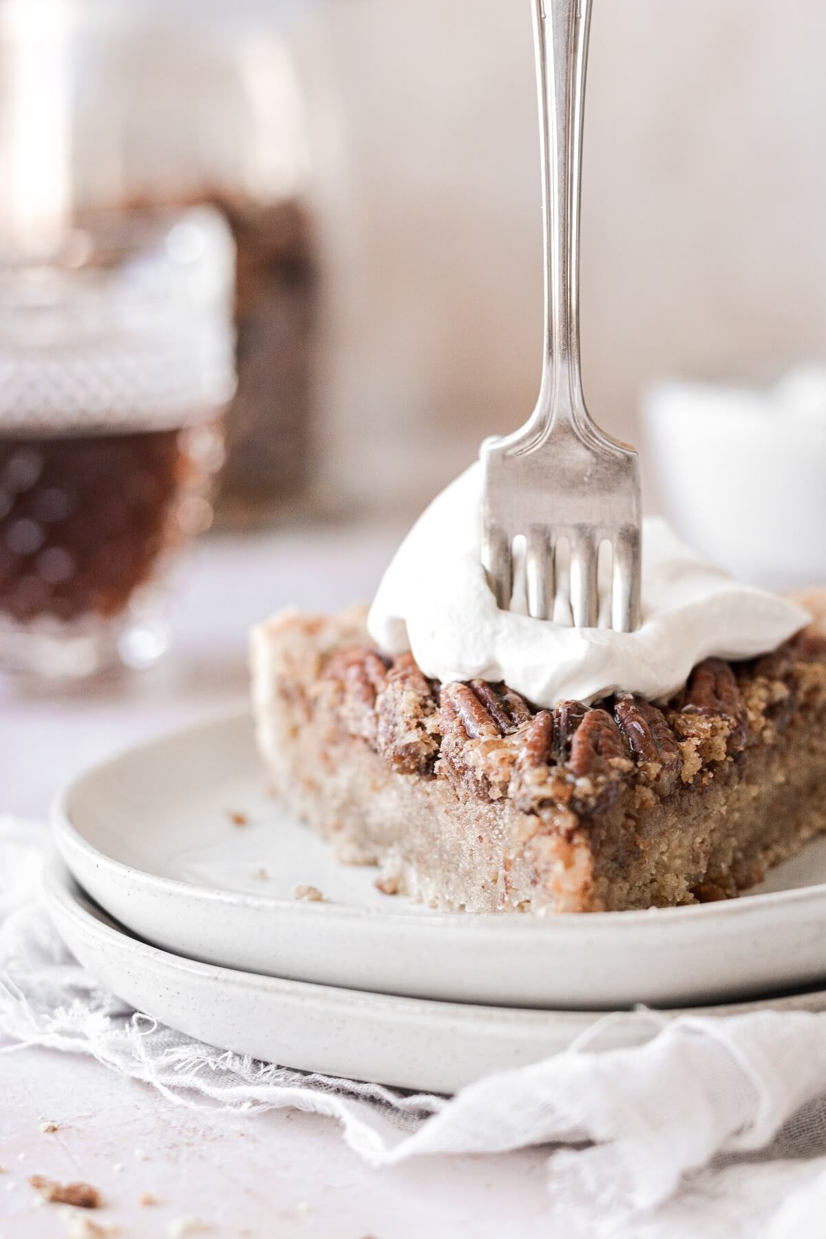 A slice of maple pecan tart topped with whipped cream.