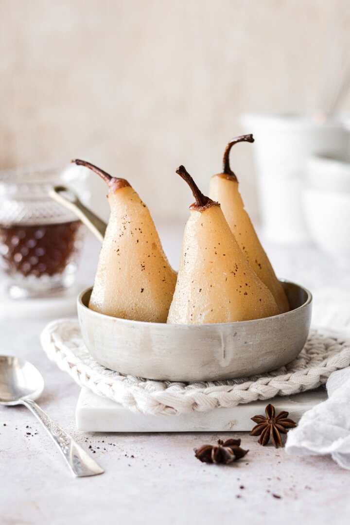 Three poached pears sitting in a pan of spiced syrup.