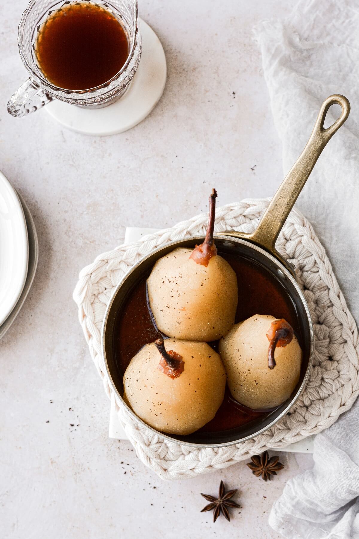 Three poached pears sitting in a pan of spiced syrup.